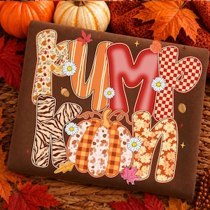 May include: A brown fabric surface featuring the word PUMPKIN in large, stylized letters. Each letter displays a unique pattern including autumn leaves, orange stripes, solid red, red checkers, zebra print, and floral designs with daisies.