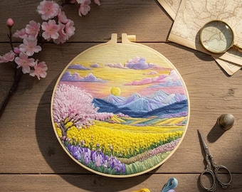 May include: A round embroidery hoop featuring a landscape scene with a yellow field, purple flowers, and blue mountains under a sunset sky. The embroidery is set on a wooden table with other craft supplies.