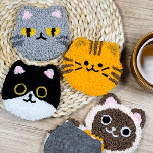 May include: Set of four handmade cat-shaped coasters. Each coaster features a different cat design, including gray, orange tabby, black and white, and brown and white. The coasters are made of a textured, looped material with felt backing.