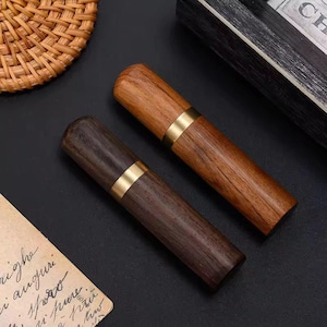 Può includere: Due porta stuzzicadenti in legno. Uno è di colore marrone chiaro, l'altro è di colore marrone scuro. Entrambi hanno una fascia color oro al centro. I supporti sono cilindrici e sembrano essere in legno lucido.