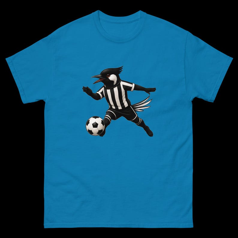 May include: A turquoise blue t-shirt featuring a cartoon bird in a soccer uniform, dribbling a soccer ball. The bird is black and white, wearing a striped jersey and shorts. The soccer ball is black and white.