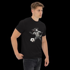 May include: Black t-shirt featuring a cartoon bird in a soccer uniform kicking a soccer ball. The bird is black and white, wearing a striped jersey. The soccer ball is black and white.