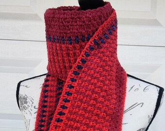 May include: A handmade, red crochet scarf with a textured pattern and dark blue trim. The scarf is displayed on a mannequin, showcasing its length and design. The scarf is approximately 72 inches long.