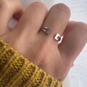 May include: A silver-toned open ring featuring two distinct triangular-shaped ends. The band is smooth and metallic, designed with a gap between the two geometric terminals, creating a modern and clean aesthetic for this finger accessory.