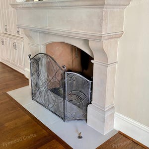 May include: A stone fireplace with a decorative metal screen. The fireplace has a light-colored stone mantel and surround. The metal screen has an ornate design. The hearth is made of light-colored stone. The floor is made of wood.
