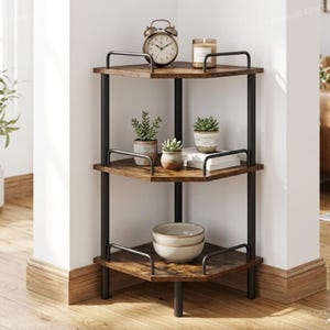 May include: A three-tiered corner shelf with a rustic, distressed wood finish and black metal frame. The top shelf holds a vintage alarm clock and a candle. The middle shelf displays potted succulents and books. The bottom shelf has a set of bowls.