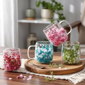Peut inclure: Quatre tasses en verre transparent remplies de fleurs séchées colorées. Une tasse contient des fleurs rouges, une autre des bleues, une troisième des vertes et la quatrième des roses. Les tasses sont sur un plateau en bois avec une petite cuillère.