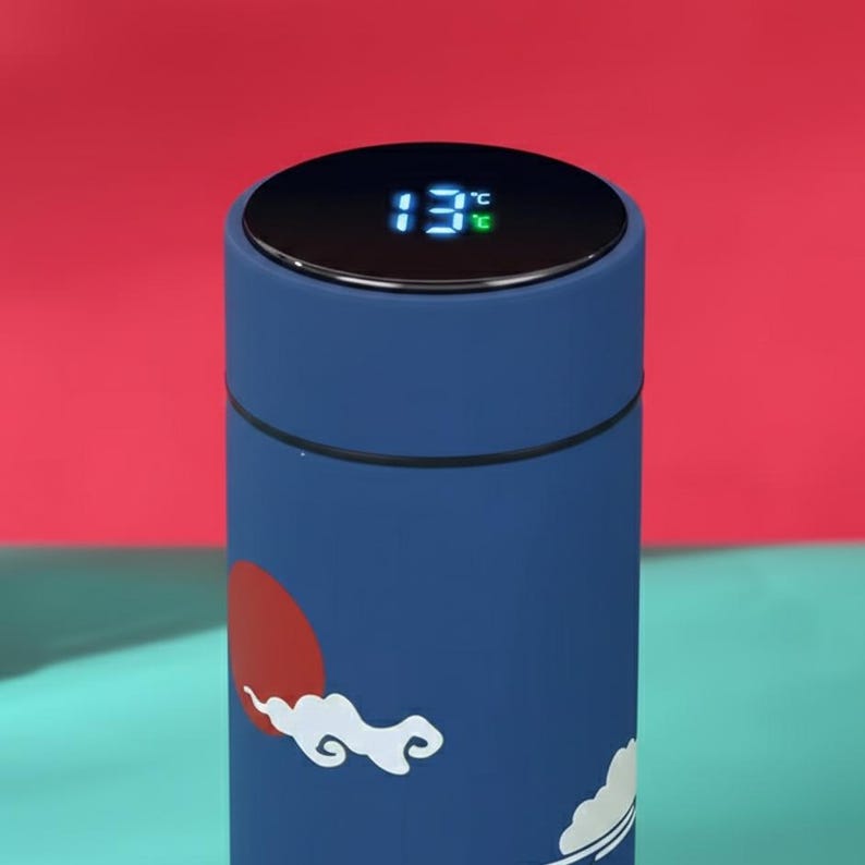 May include: A blue insulated tumbler with a digital temperature display showing 13&deg;C. The tumbler features a design with a red sun and white clouds. The background is a mix of red and teal.