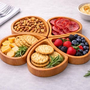 Könnte beinhalten: Ein hölzernes Serviertablett mit fünf Abschnitten, die jeweils mit verschiedenen Snacks gefüllt sind. Die Abschnitte enthalten Nüsse, geschnittene Salami, Cracker, Käsewürfel und frische Beeren. Oliven, Hummus und Brotstangen sind ebenfalls vorhanden.