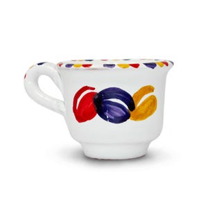 Può includere: Una tazza in ceramica bianca con un disegno dipinto a mano composto da tre audaci pennellate a spirale in rosso, blu scuro e giallo sulla parte anteriore. Il bordo è decorato con un motivo ripetitivo di piccoli punti colorati in rosso, blu e giallo.