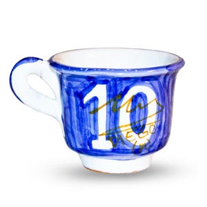 Può includere: Una tazza da caffè in ceramica bianca con un disegno dipinto di blu. La tazza presenta il numero "10" in bianco, con dettagli dorati e il nome "DIEGO" scritto sotto. Il manico è bianco.