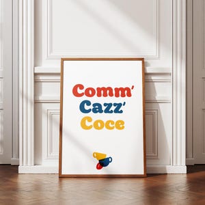 Può includere: Una stampa artistica incorniciata con le parole "Comm' Cazz' Coce" in rosso, blu e giallo, con tre tazze di caffè stilizzate in basso. La stampa è in una cornice di legno marrone, su una parete bianca e un pavimento in legno.
