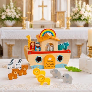 Könnte beinhalten: Ein hölzernes Arche Noah Spielset mit einem Boot mit Regenbogen-Dach, zwei menschlichen Figuren und verschiedenen Tierfiguren wie Zebras, Bären, Löwen, Elefanten und einem Krokodil. Das Boot ist mit dem Text Matteo Zur Taufe 10.05.2026 personalisiert.