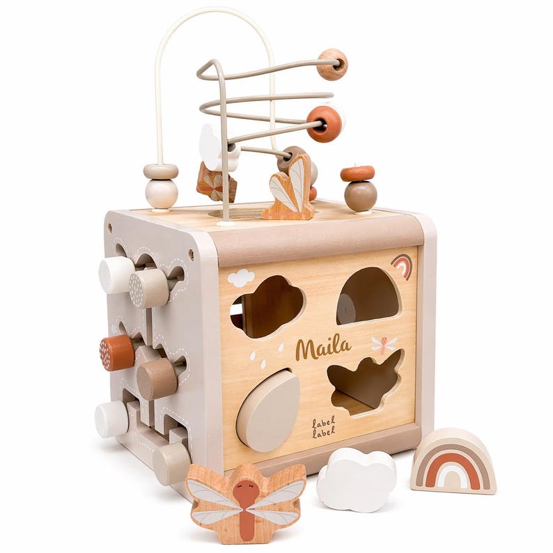 May include: A wooden activity cube with a bead maze, shape sorter, and various interactive elements. The cube features a neutral colour palette with accents of brown, beige, and white. The name "Maila" is printed on the side, along with cloud and rainbow designs.