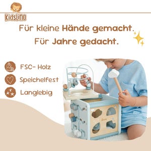 May include: A wooden activity cube in light blue and natural wood. It includes a bead maze, shape sorters, and other interactive features. The text "KidsLino" and "Liane" are visible. Designed for small hands, the cube is a children's toy.