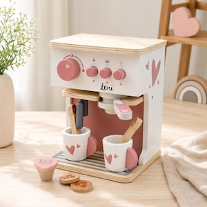 Può includere: Macchina da caffè giocattolo in legno bianca e rosa, con il nome "Leni" stampato. Include due tazze con cuori, cucchiai di legno e gettoni a forma di chicco di caffè. Un giocattolo divertente per bambini.