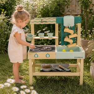 Könnte beinhalten: Eine hölzerne Outdoor-Spielküche mit einem hellgrünen Waschbecken und einer Arbeitsplatte sowie einem Wasserspiel. Die Spielküche hat ein Regal mit kleinen grünen Töpfen und ein unteres Regal mit Kochutensilien. Der Name "Lina" steht oben.