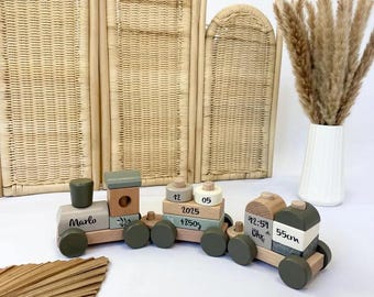 May include: A wooden toy train in olive green and natural wood. The train cars feature stacked blocks with the name "Marlo" and other details. The train is a decorative item.