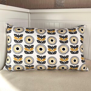May include: Rectangular decorative pillow with a white background and a repeating pattern of yellow, black, and gray floral designs. The pillow is placed on a neutral-colored surface.