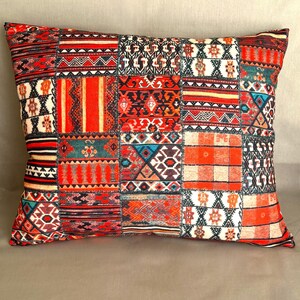 Puede incluir: Coj&iacute;n decorativo rectangular con dise&ntilde;o de patchwork. El coj&iacute;n presenta una variedad de patrones en rojo, naranja, turquesa y blanco. Los patrones incluyen formas geom&eacute;tricas, rayas y motivos florales. El coj&iacute;n est&aacute; colocado sobre una superficie de color neutro.