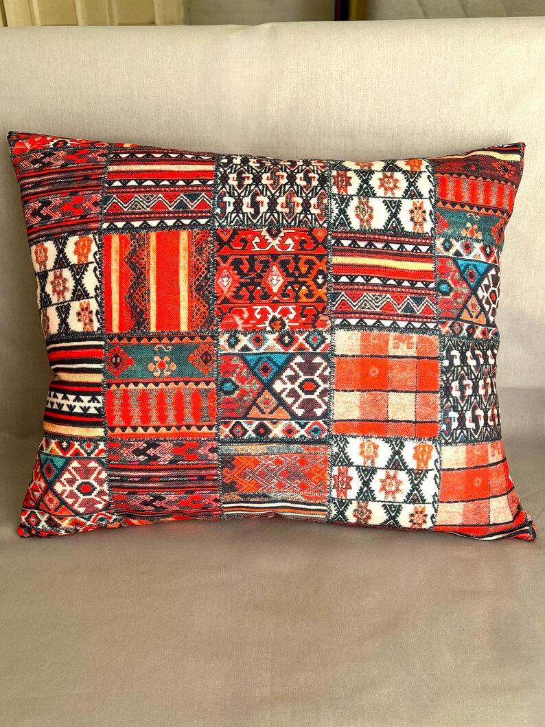 Puede incluir: Coj&iacute;n decorativo rectangular con dise&ntilde;o de patchwork. El coj&iacute;n presenta una variedad de patrones en rojo, naranja, turquesa y blanco. Los patrones incluyen formas geom&eacute;tricas, rayas y motivos florales. El coj&iacute;n est&aacute; colocado sobre una superficie de color neutro.