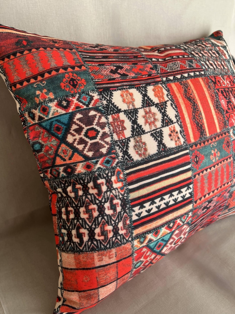 Puede incluir: Un coj&iacute;n cuadrado con un dise&ntilde;o de patchwork. El coj&iacute;n presenta una variedad de patrones geom&eacute;tricos en tonos de rojo, naranja, verde azulado y negro. El coj&iacute;n parece estar hecho de una tela suave.