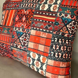 Puede incluir: Coj&iacute;n rectangular decorativo con dise&ntilde;o de patchwork. El coj&iacute;n presenta una vibrante mezcla de patrones en rojo, naranja, turquesa y negro. El dise&ntilde;o incluye formas geom&eacute;tricas, rayas y motivos florales, creando una apariencia texturizada y colorida.