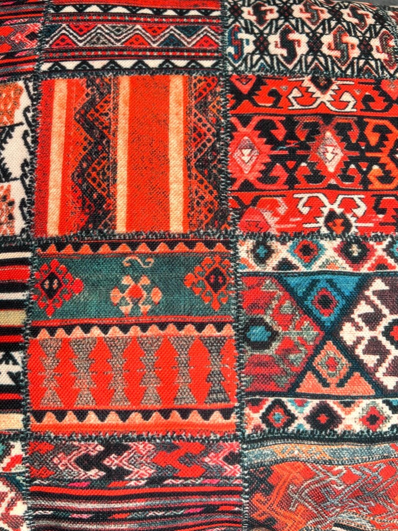 Puede incluir: Primer plano de un textil patchwork con una vibrante mezcla de colores y patrones. El dise&ntilde;o presenta cuadrados con motivos geom&eacute;tricos y tribales en tonos de rojo, naranja, verde azulado, negro y blanco. La tela tiene una apariencia texturizada.