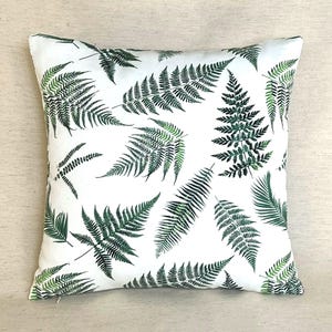 May include: A square throw cushion featuring a white background with a repeating pattern of dark green fern leaves. The botanical print displays various sizes and orientations of fern fronds scattered across the entire surface of the cushion cover.