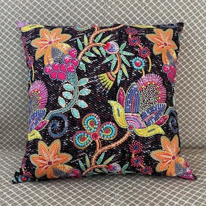 Könnte beinhalten: Quadratisches Zierkissen mit schwarzem Hintergrund und farbenfrohem Blumenmuster. Die Blumen sind in Orange-, Rosa-, Blau- und Gelbtönen gehalten. Das Kissen hat eine Paillettenstruktur.