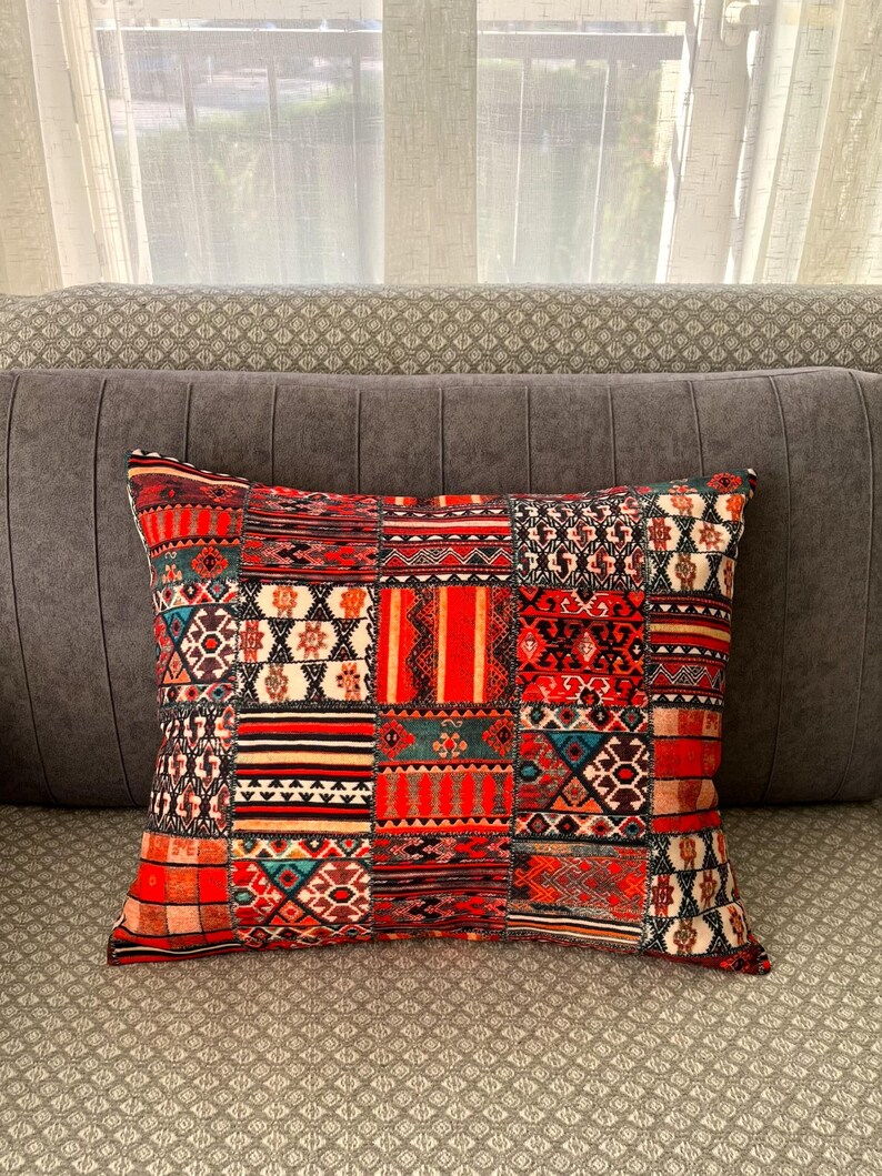Puede incluir: Coj&iacute;n decorativo rectangular con dise&ntilde;o de patchwork. El coj&iacute;n presenta una variedad de patrones en rojo, naranja, negro y turquesa. El coj&iacute;n est&aacute; colocado sobre un sof&aacute; gris.