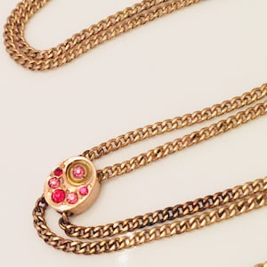 May include: A gold chain necklace with a circular pendant featuring a cluster of pink gemstones.