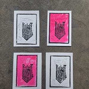May include: Four art prints with a linocut design. Two prints are black and white, and two are pink with a black design. Each print features the word "PERSIST" above a stylized shield shape.