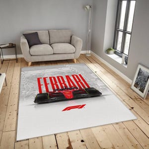 Könnte beinhalten: Rechteckiger Teppich mit einem roten Ferrari Formel 1-Auto-Design. Das Wort "FERRARI" ist rot gedruckt. Der Teppich hat einen weißen Hintergrund mit einem grauen Rand. Geeignet für das Wohnzimmer.