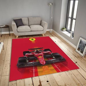 Könnte beinhalten: Ein roter rechteckiger Teppich mit einem Formel-1-Rennwagen-Design. Der Teppich hat einen roten Hintergrund mit einem gelb-orangen Streifeneffekt. Der Rennwagen ist rot und schwarz, mit dem Ferrari-Logo oben.