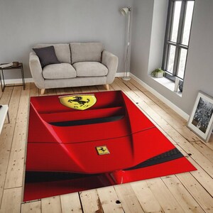 May include: A rectangular red rug featuring a close-up of a Ferrari car design. The rug has a glossy finish and includes the Ferrari logo in yellow and black. The rug is placed on a wooden floor.