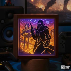 Könnte beinhalten: Eine Holz-Leuchtbox mit einer Silhouette einer Figur, die eine Waffe hält, vor einer Wüstenlandschaft mit einem Schild "Welcome to New Vegas". Das Kunstwerk wird in Orange, Lila und Blau beleuchtet, was einen auffälligen visuellen Effekt erzeugt.