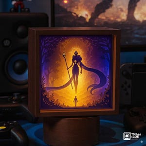 Könnte beinhalten: Eine Holz-Leuchtbox mit einer geschichteten Papierkunstszene. Das Kunstwerk zeigt eine Silhouette mit Stab, Heiligenschein und Umhang, über einer kleineren Figur. Der Hintergrund wechselt von Gelb zu Blau, mit Bäumen und Laub.