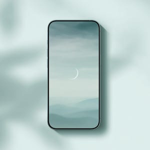 May include: A smartphone with a silver frame displays a serene landscape with a crescent moon. The screen shows a gradient of blue and gray hues, suggesting a mountain range under a cloudy sky. The phone is centered on a light blue surface.