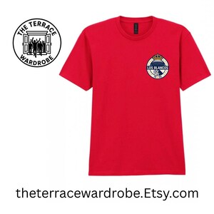 May include: A red t-shirt with a crew neck and short sleeves. The shirt features a small emblem on the left chest with the text "LOS BLANCOS" and "1902". The Terrace Wardrobe logo is on the left side. The website address is at the bottom.