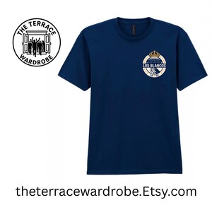 May include: Navy blue t-shirt with a circular logo featuring a crown and the text "LOS BLANCOS 19-02". The shirt also has a logo on the upper left corner that says "THE TERRACE WARDROBE".
