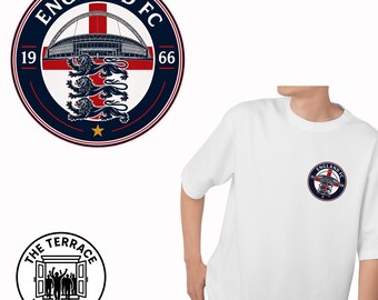 Puede incluir: Una camiseta blanca de manga corta con un logotipo circular de England FC en el pecho. El logo muestra un estadio, tres leones, el texto England FC, los años 19 y 66, y una estrella dorada. Un logo circular secundario muestra el texto The Terrace Wardrobe.