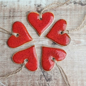 May include: Five red ceramic heart ornaments with a rustic finish, each with a hole for hanging and a twine string attached.