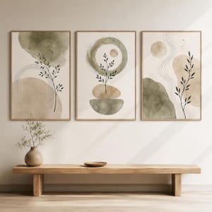 May include: A set of three framed wall art prints featuring abstract watercolour shapes in sage green and beige. Each print displays delicate black line drawings of botanical stems, curved lines, and circular forms on a neutral off-white background.