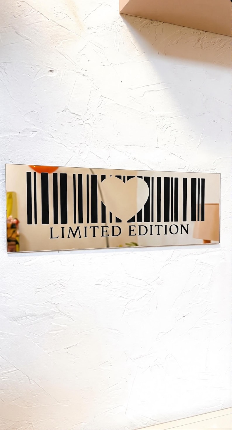 May include: A rectangular mirror with a heart-shaped cutout and a barcode design. The words "LIMITED EDITION" are printed in black below the barcode. The mirror is mounted on a textured white wall.