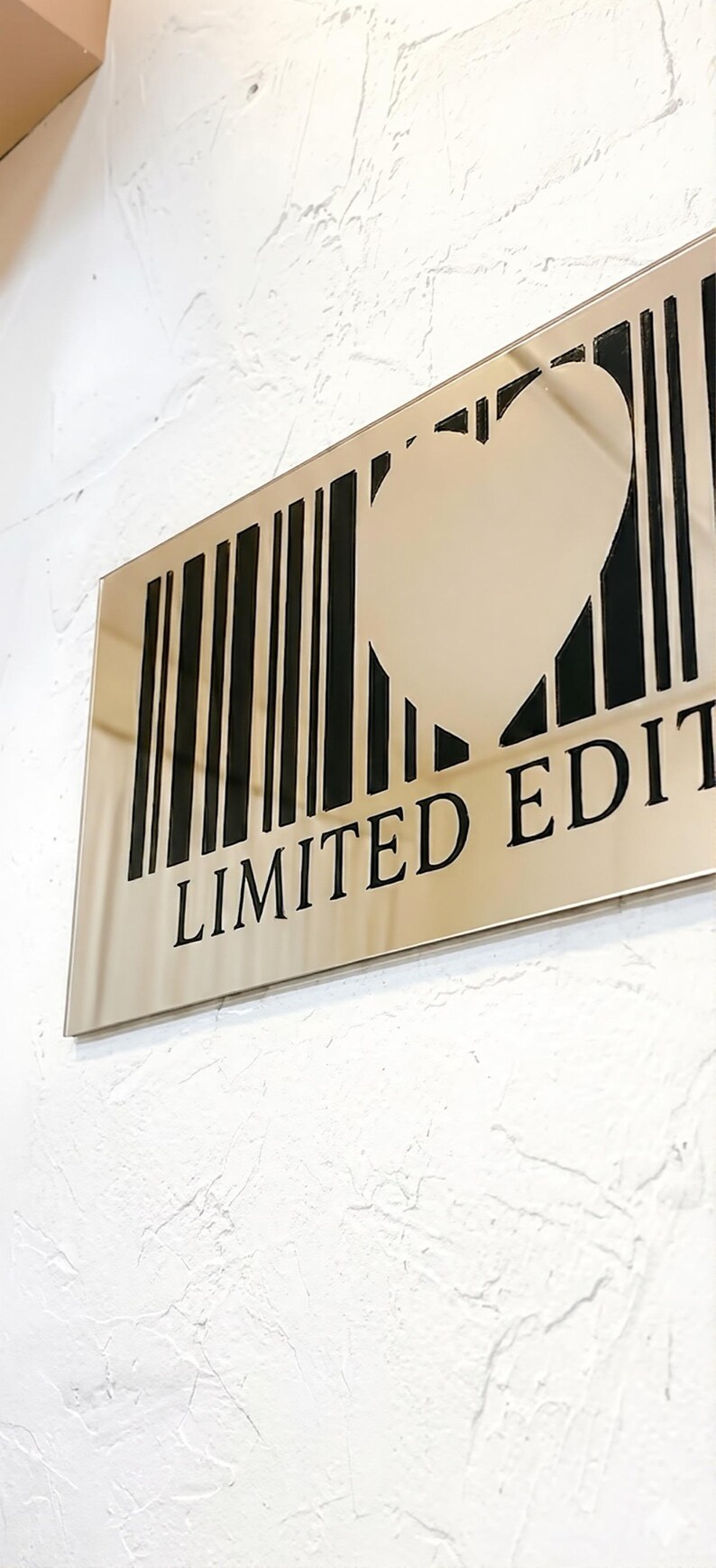 May include: A rectangular, metallic sign with a heart-shaped cutout within a barcode design. The words "LIMITED EDITION" are printed in black below the barcode. The sign is mounted on a textured white wall.