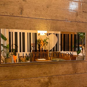 May include: A rectangular mirror with a barcode design and the words "LIMITED EDITION" in black. The mirror is mounted on a wooden wall. The barcode design includes a heart shape.