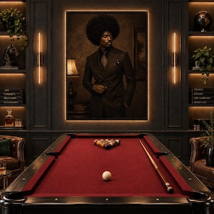 May include: A pool table with a deep red felt surface, a white cue ball, a rack of colorful billiard balls, and a wooden cue stick. Above the table hangs a large portrait of a person with an afro wearing a dark double-breasted suit jacket.