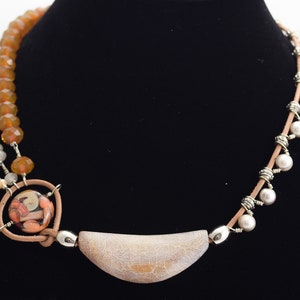 May include: A multi-strand necklace featuring brown, white and cream beads, a large cream-coloured pendant, and a smaller pendant with a colourful glass design.