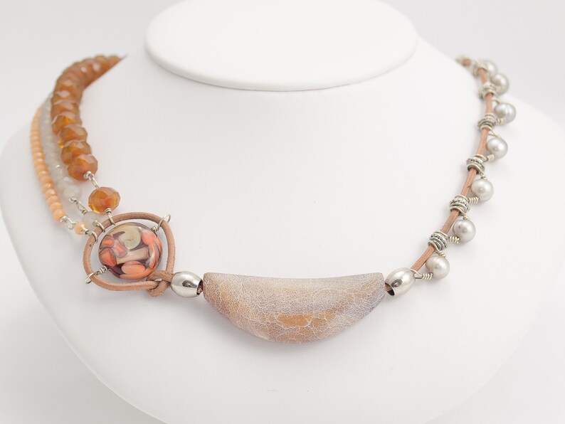 May include: A multi-strand necklace featuring brown, beige and white beads, a large agate pendant and silver accents.